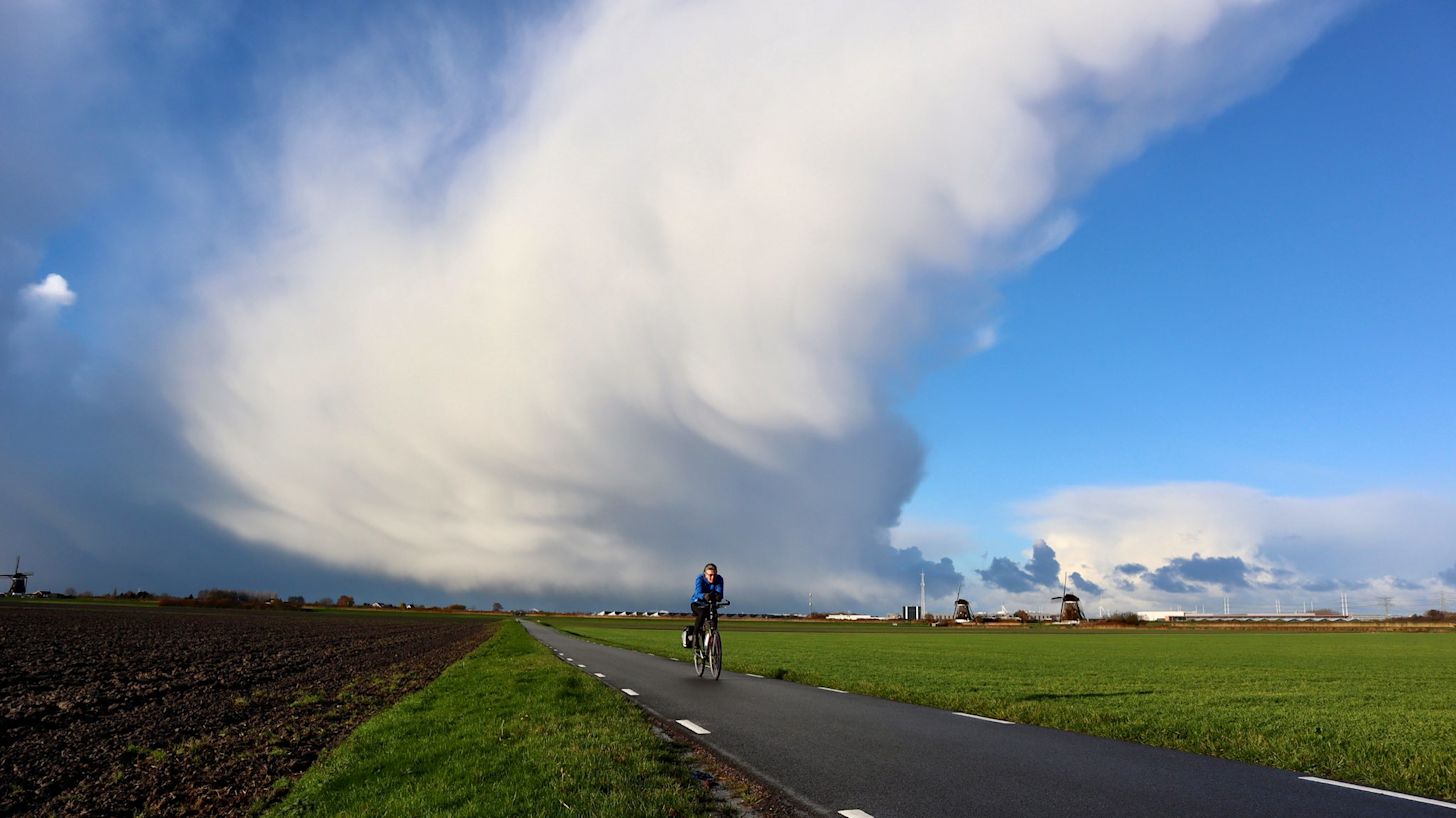 Fietser met winterse bui op de achtergrond in Hollands landschap