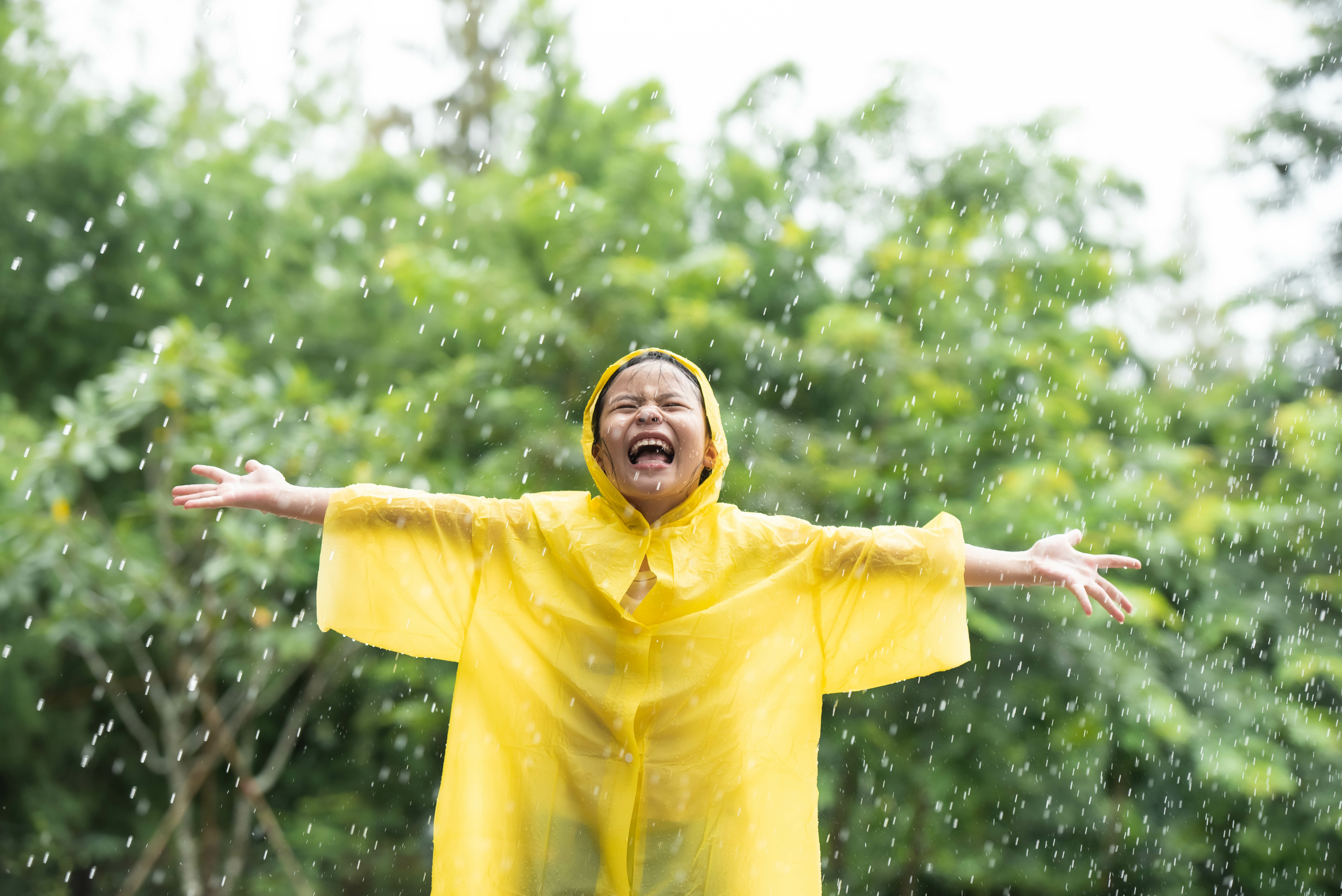 Meisje in gele poncho geniet van de regen in wisselvallig weekend