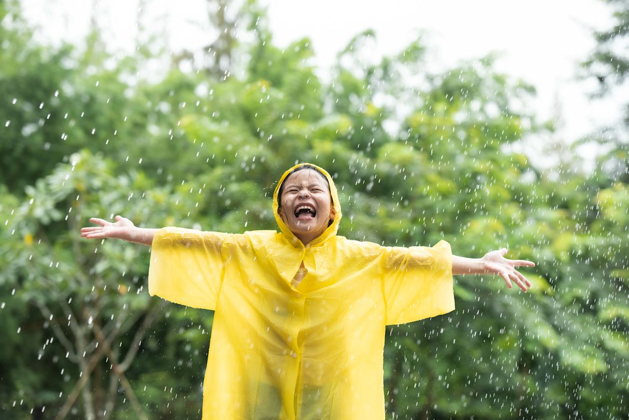Meisje in gele poncho geniet van de regen in wisselvallig weekend