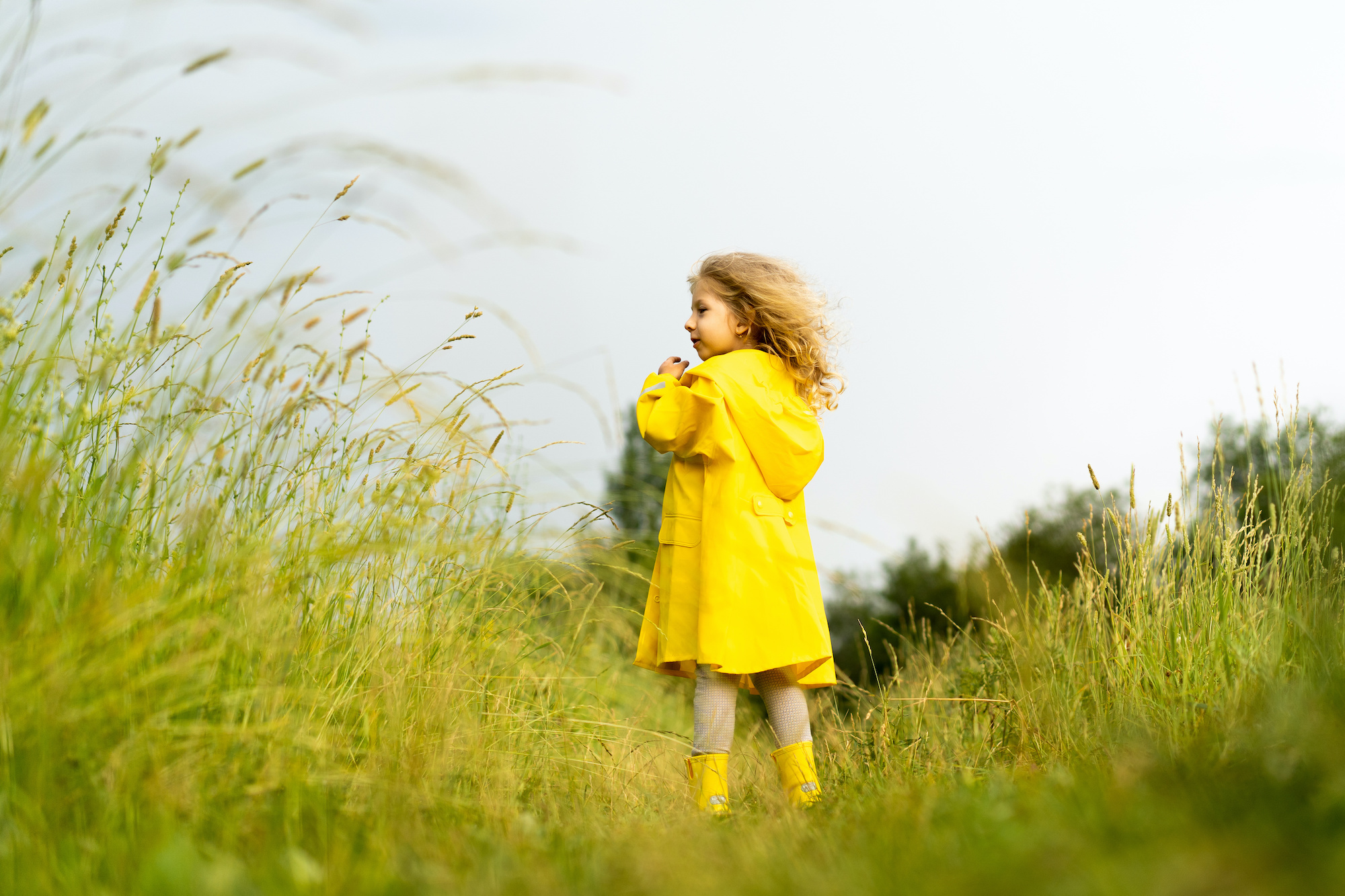 Meisje met gele regenjas geniet tussen het hoge gras van mooi weer