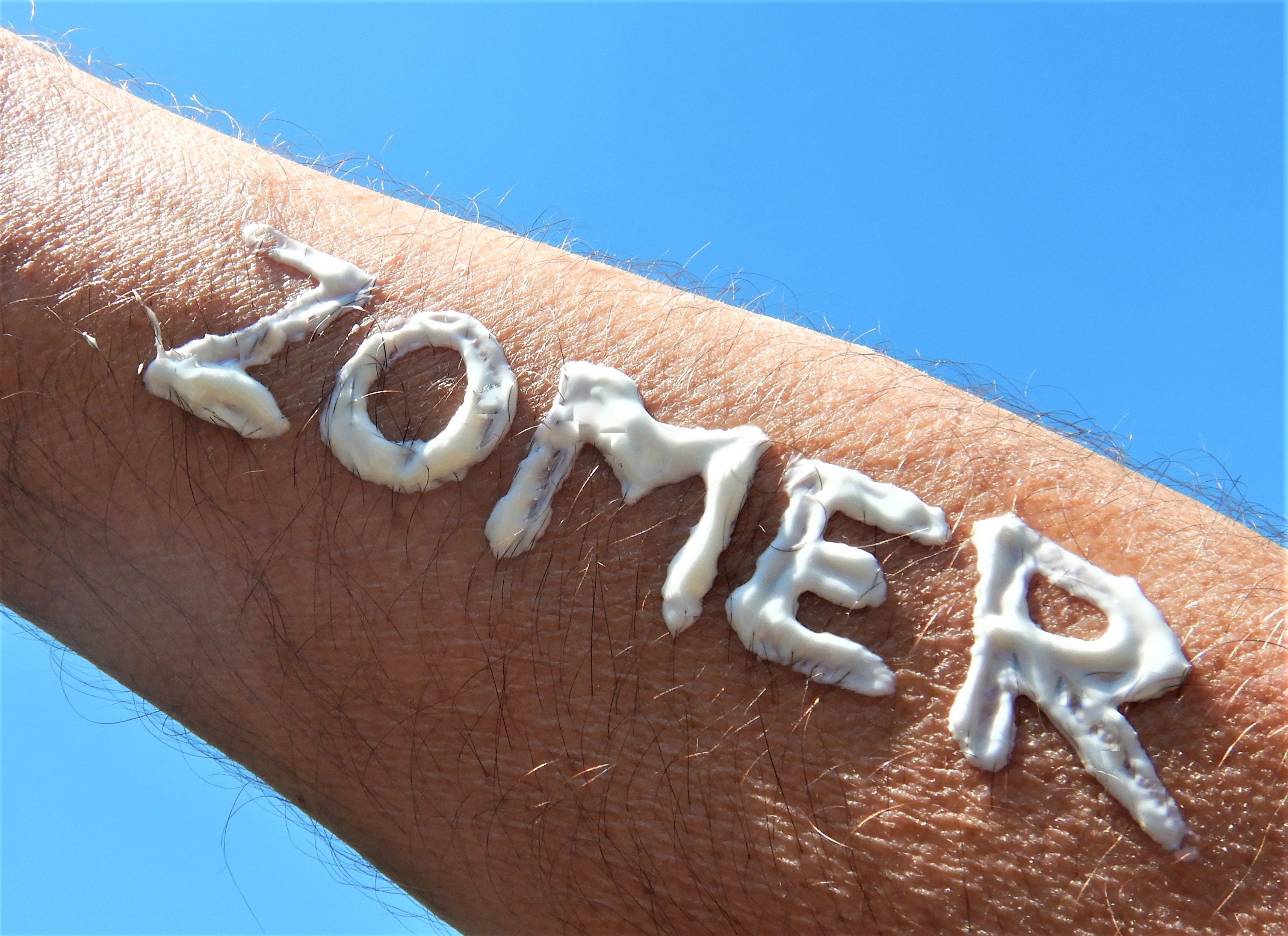 Woord zomer geschreven met zonnebrandcrème op iemands arm - het is een zomerse dag met 25 graden begin juni