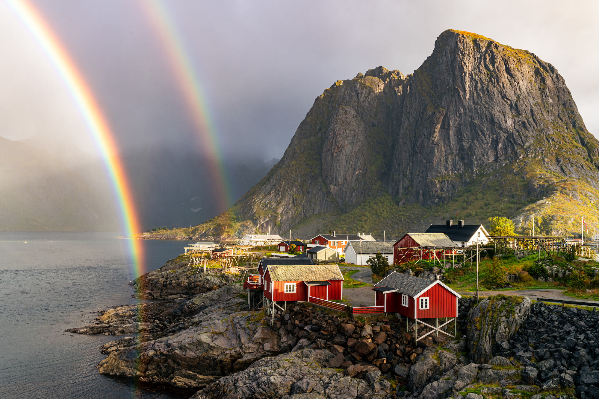 Dubbele regenboog bij de Lofoten in Noorwegen met typische rode houten huizen en bergen op de achtergrond