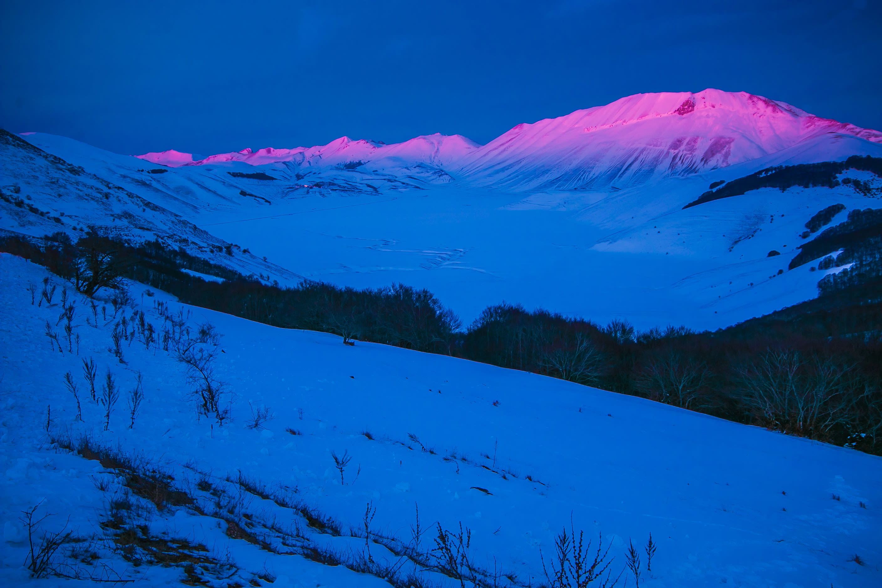 Besneeuwde bergtoppen lichten op terwijl de zon al onder is. Foto: Adobe Stock / Buffy1982