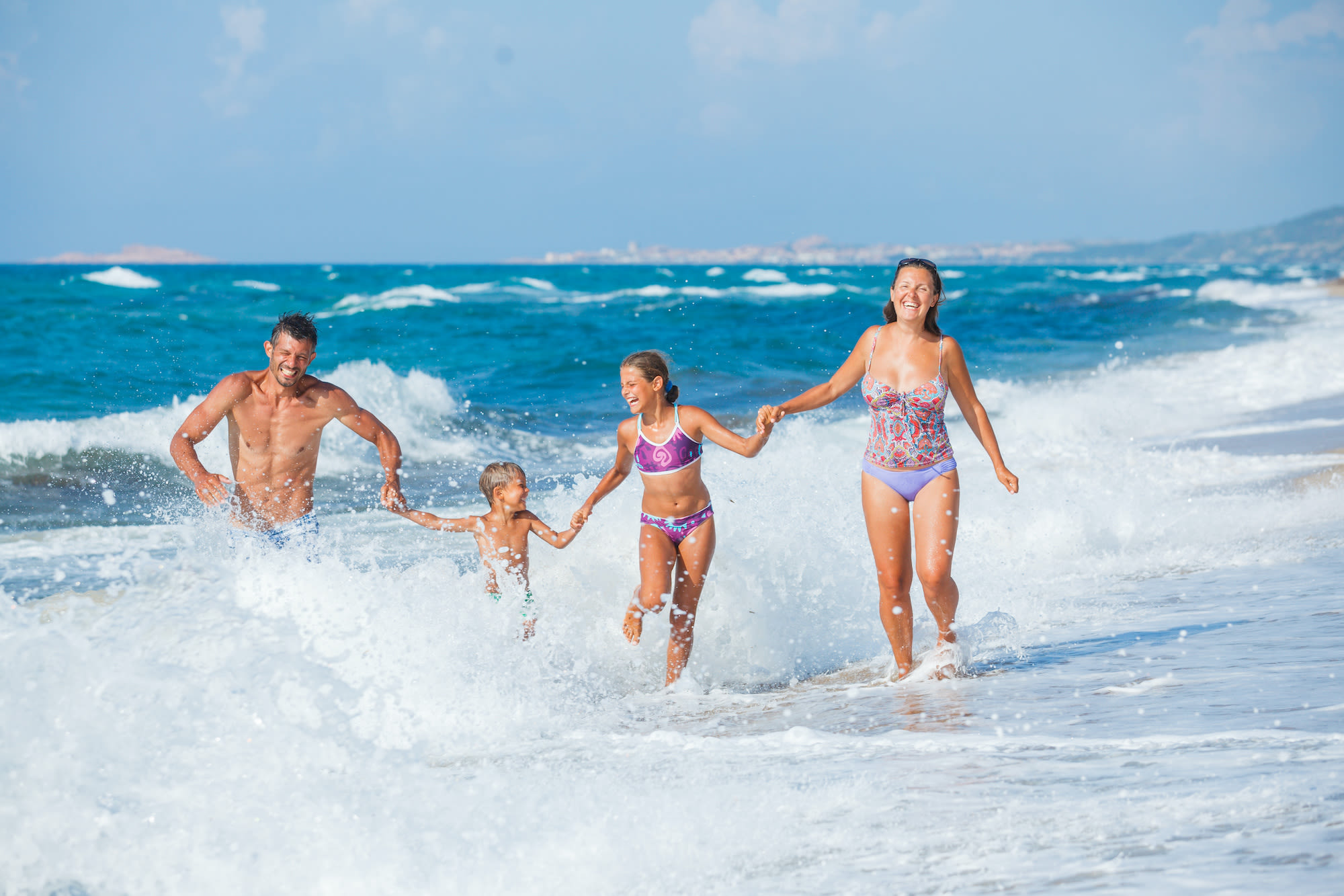 Familie met twee kinderen heeft plezier in de golven van de Middellandse Zee.  Foto: Adobe Stock / Max Topchii