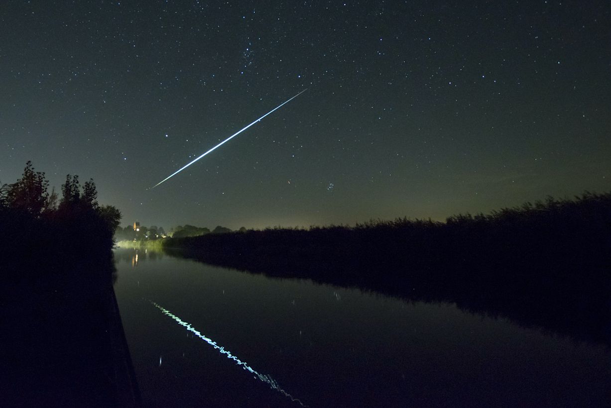Extreem mooie vallende ster tijdens heldere nacht in de zomer boven een stil wateroppervlak