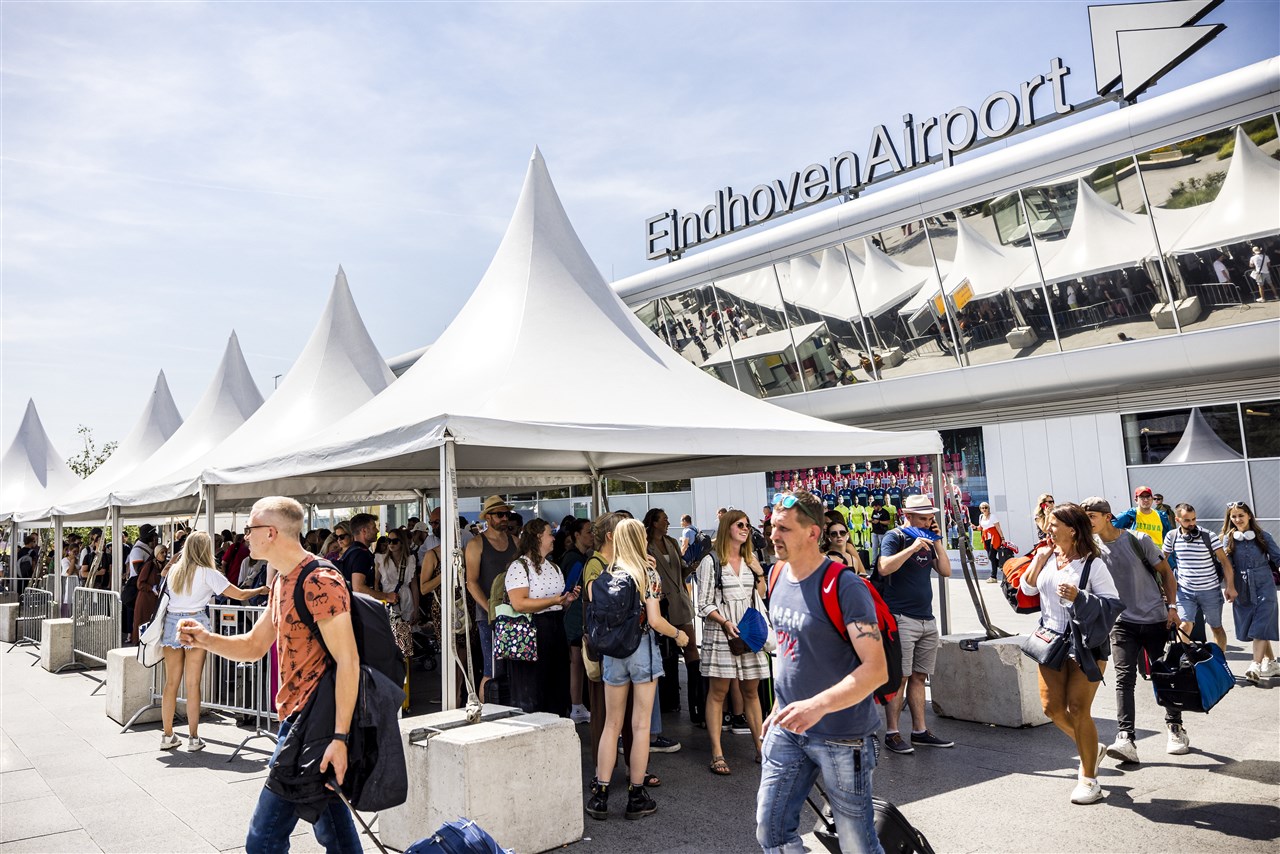 Medewerkers van Eindhoven Airport delen waaiers uit aan reizigers die staan te wachten in de hitte.
 Foto: ANP / ROB ENGELAAR