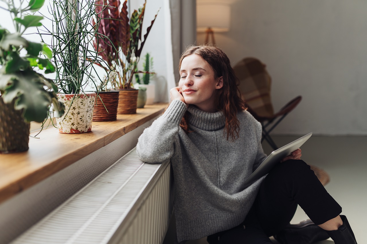 Vrouw geniet voor het raam van de binnenkomende zonnestralen. Foto: Adobe Stock / contrastwerkstatt