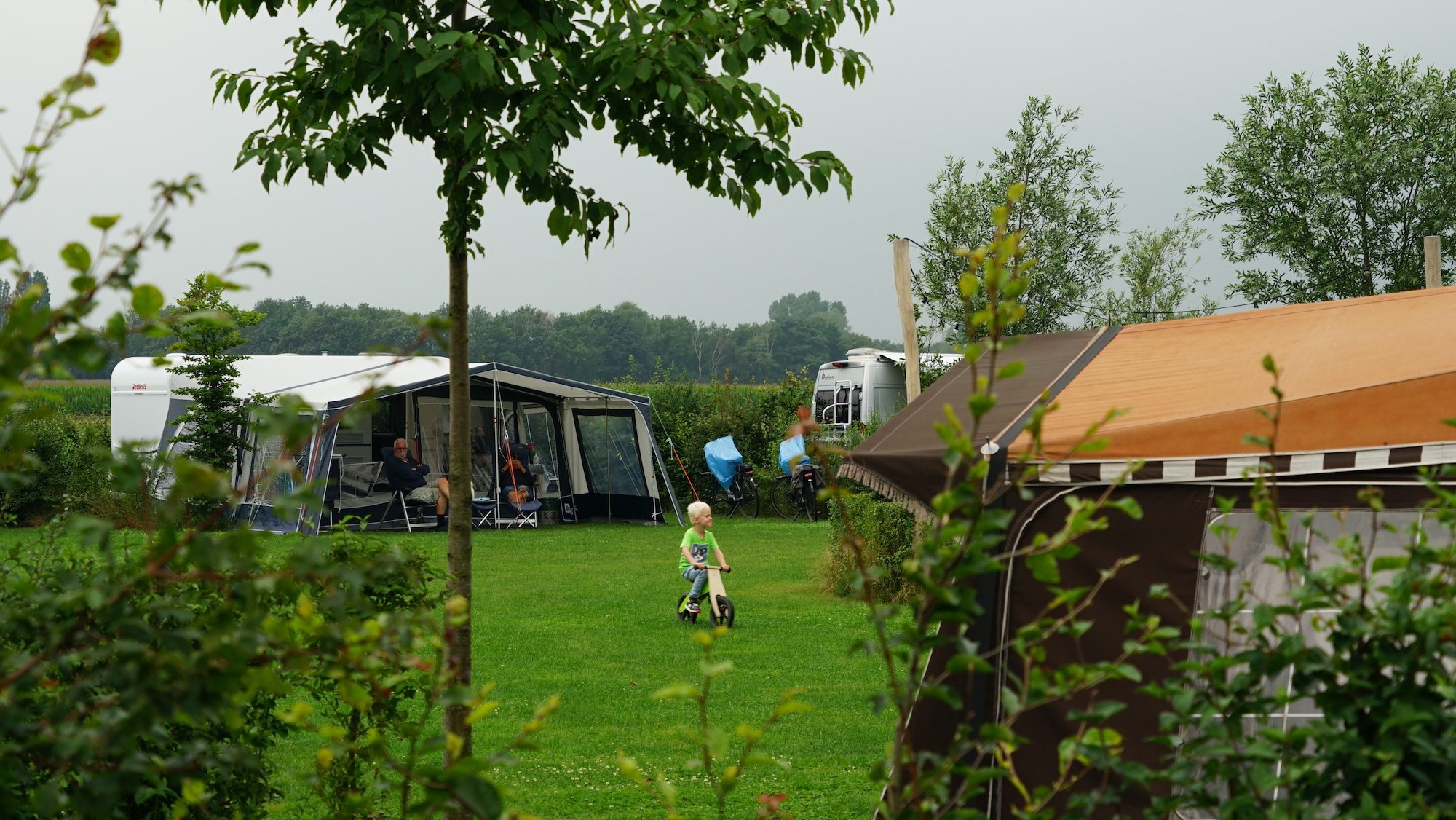 Kindje op fiets bij grijs en wisselvallig weer op de camping