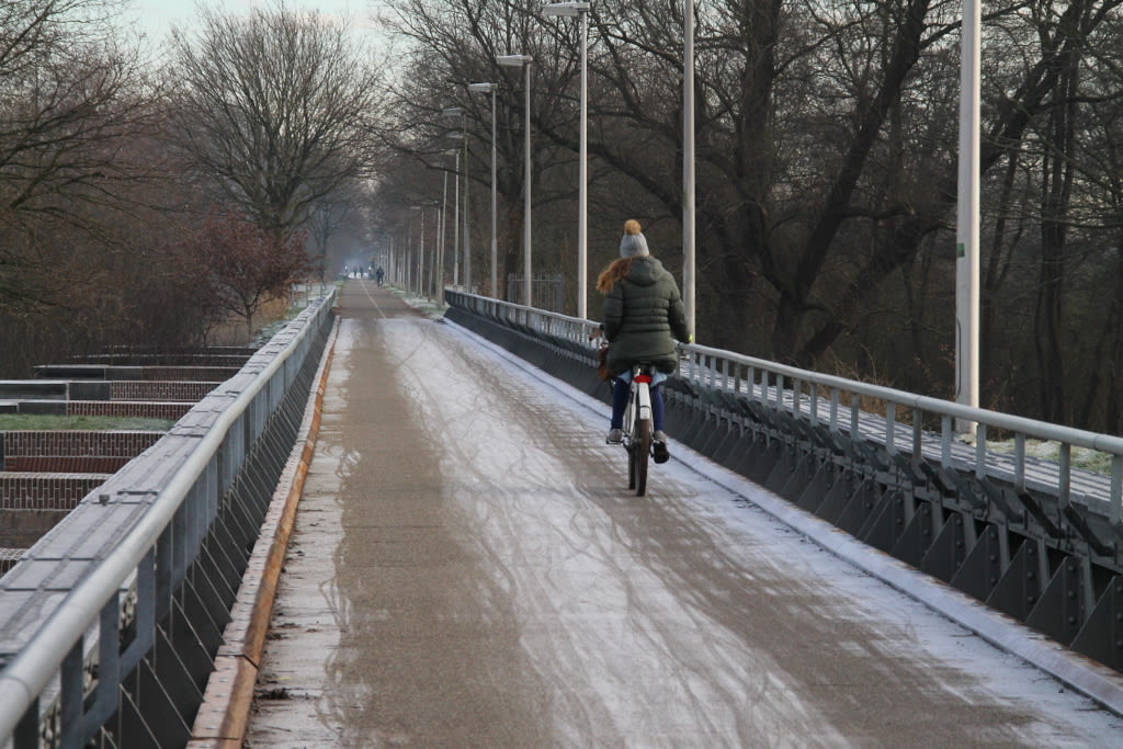 Vrouw op fiets met muts op gladde brug koud winterweer